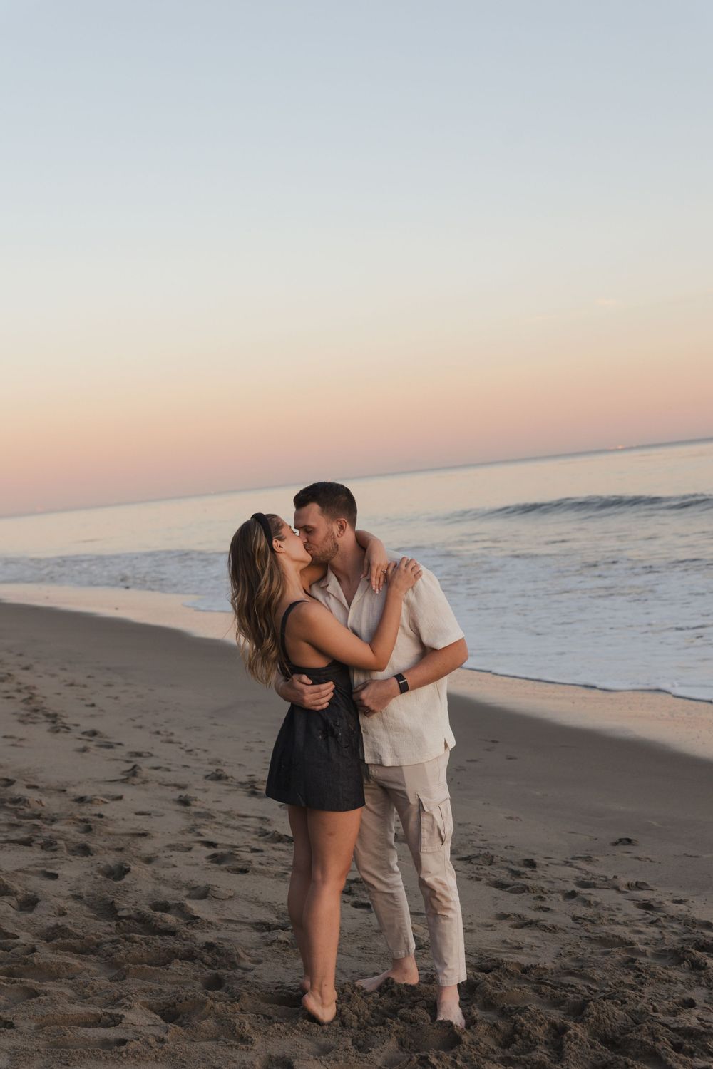 A couple sharing a romantic embrace on a sandy beach at dusk.