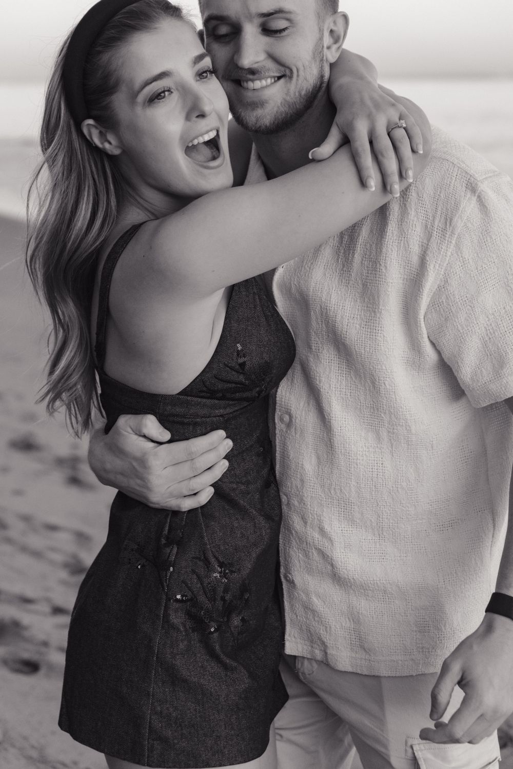 Joyful couple laughing and hugging together during a beach photoshoot.