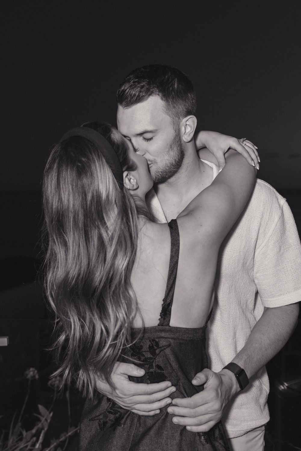 A romantic black and white photo of a couple sharing an intimate embrace in casual attire.