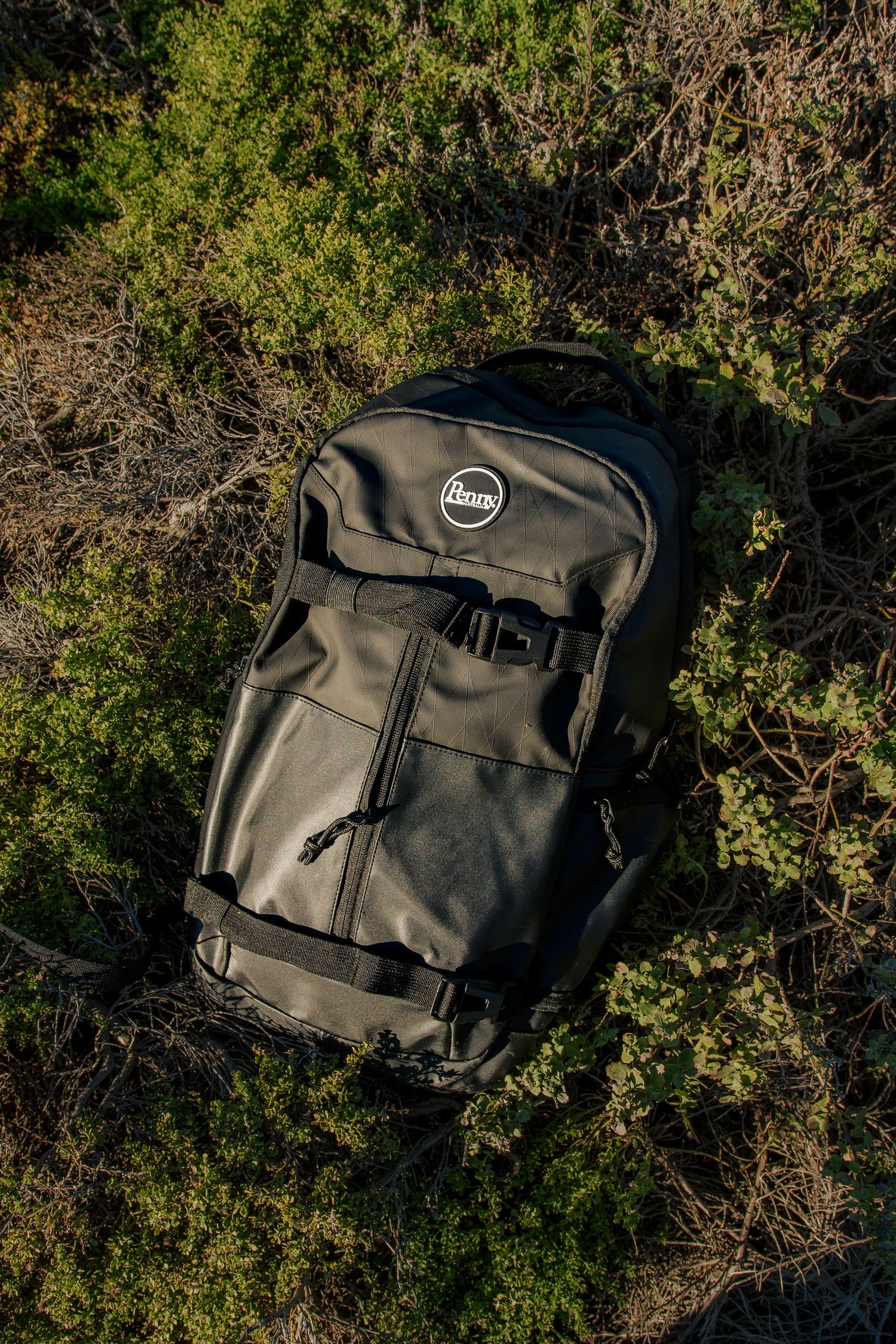 Black adventure backpack lying on coastal brush and vegetation against natural outdoor setting.