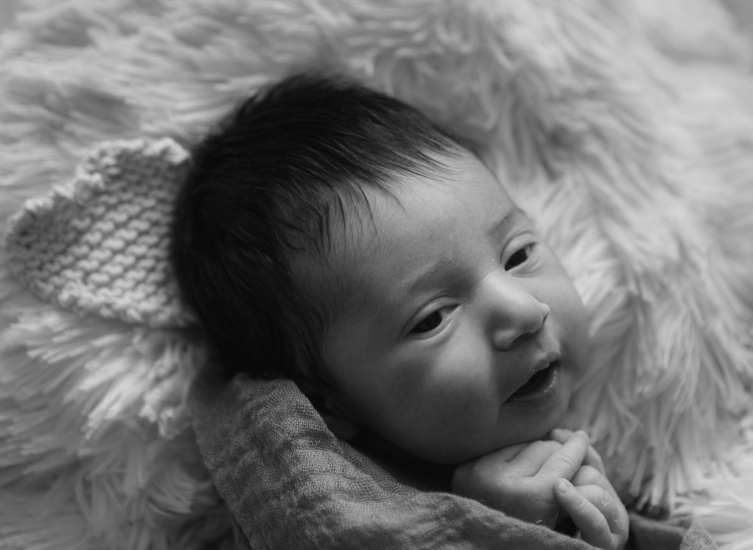 Black and white portrait of smiling baby wrapped in knitted blanket.