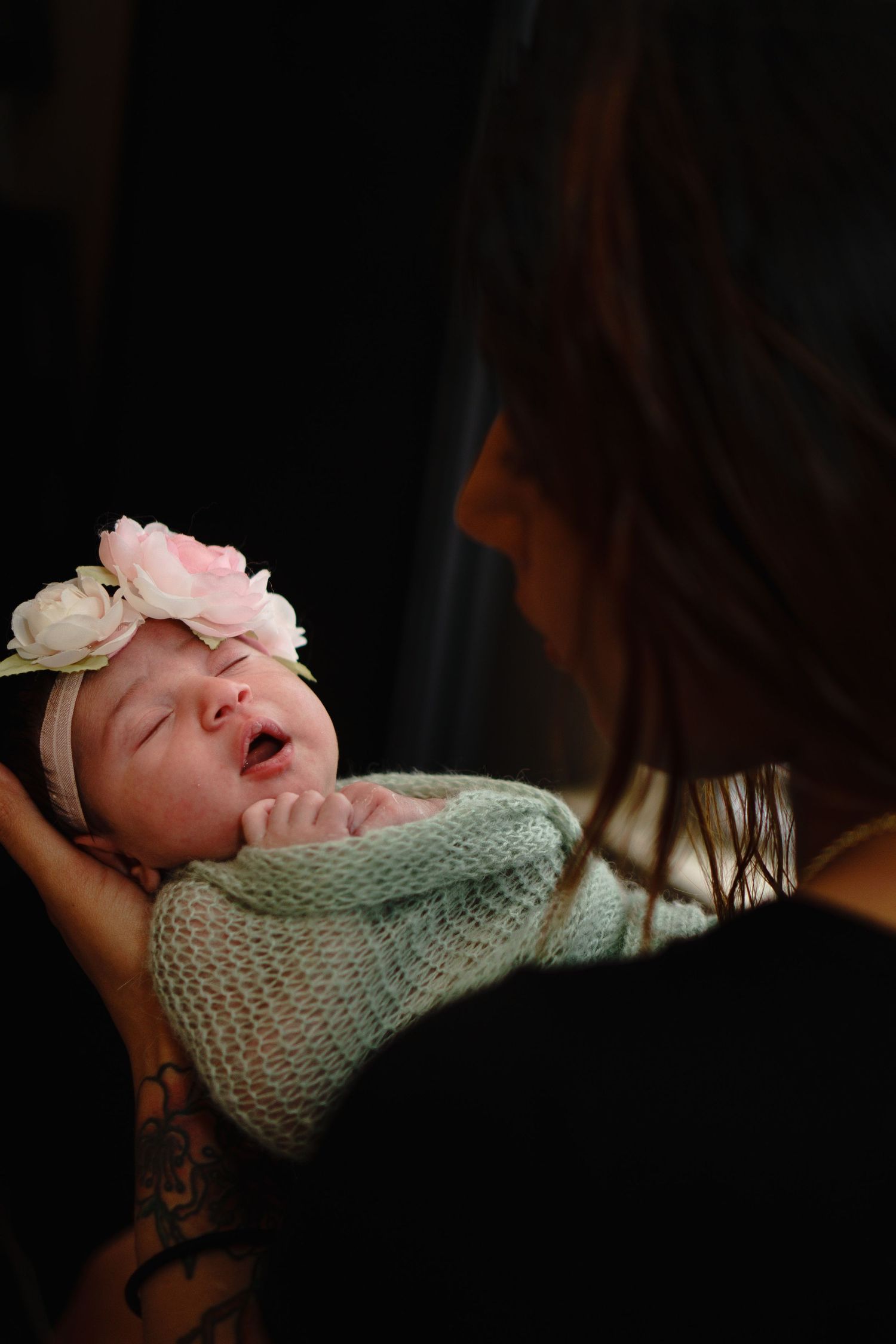 Newborn baby wearing floral headband and knit sweater being cradled.