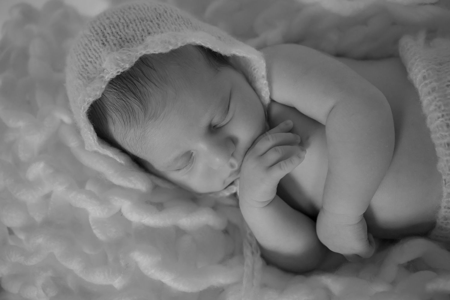 Sleeping newborn wrapped in soft white blankets in black and white portrait.