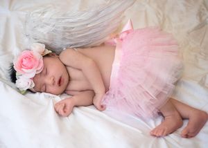 Sleeping baby in pink tutu with floral headpiece on white bedding.