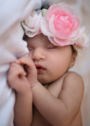 Peaceful sleeping baby wearing pink rose crown against white fabric.