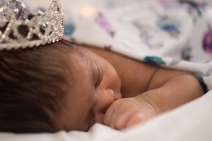 Sleeping baby wearing sparkly crown against floral bedding.