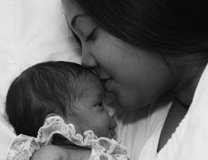 An intimate black and white photograph showing a mother's gentle kiss on her baby's face.