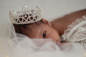 Baby wearing delicate crystal tiara nestled in white lace.