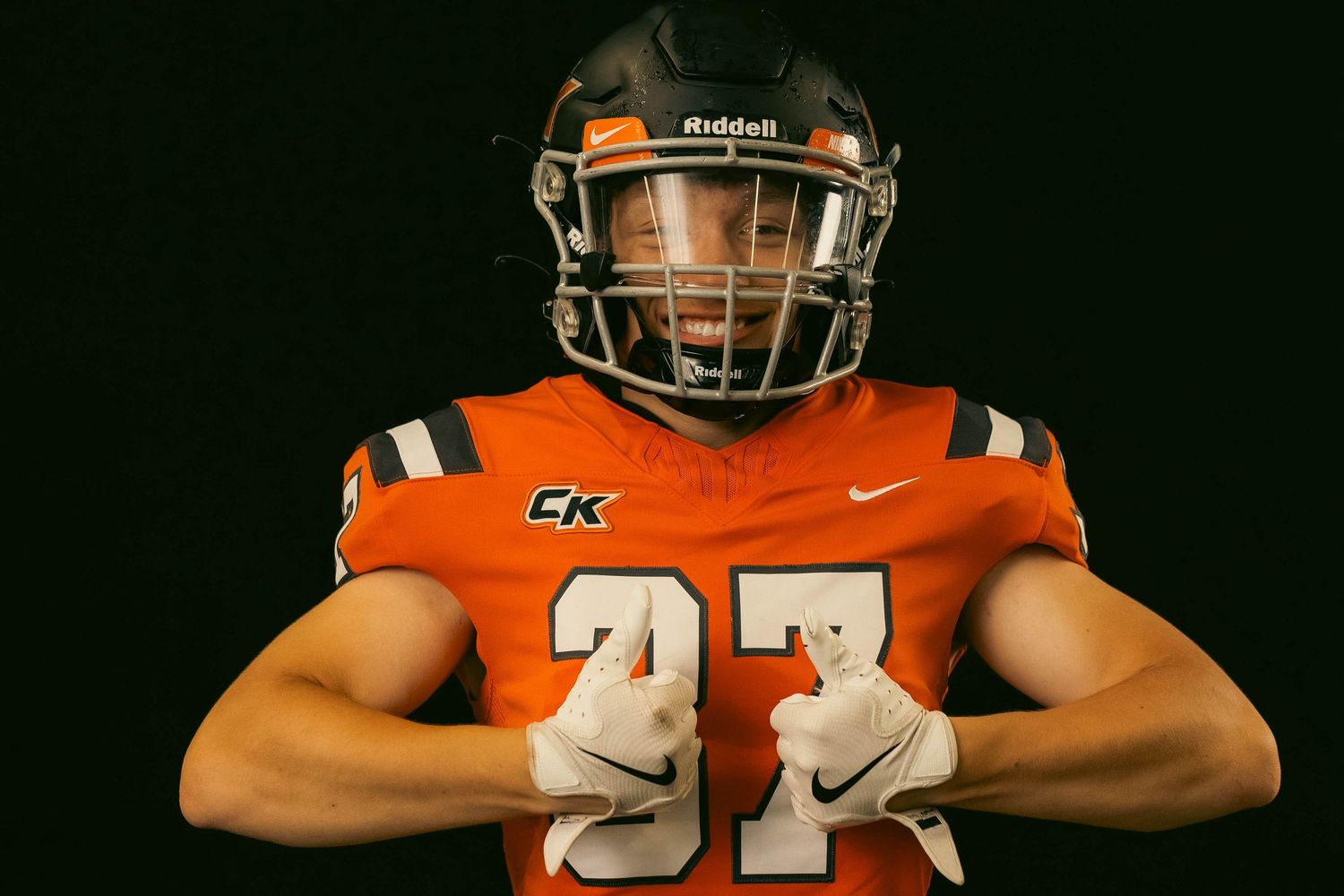 College football player in orange jersey number 47 poses with arms crossed in dark studio setting.
