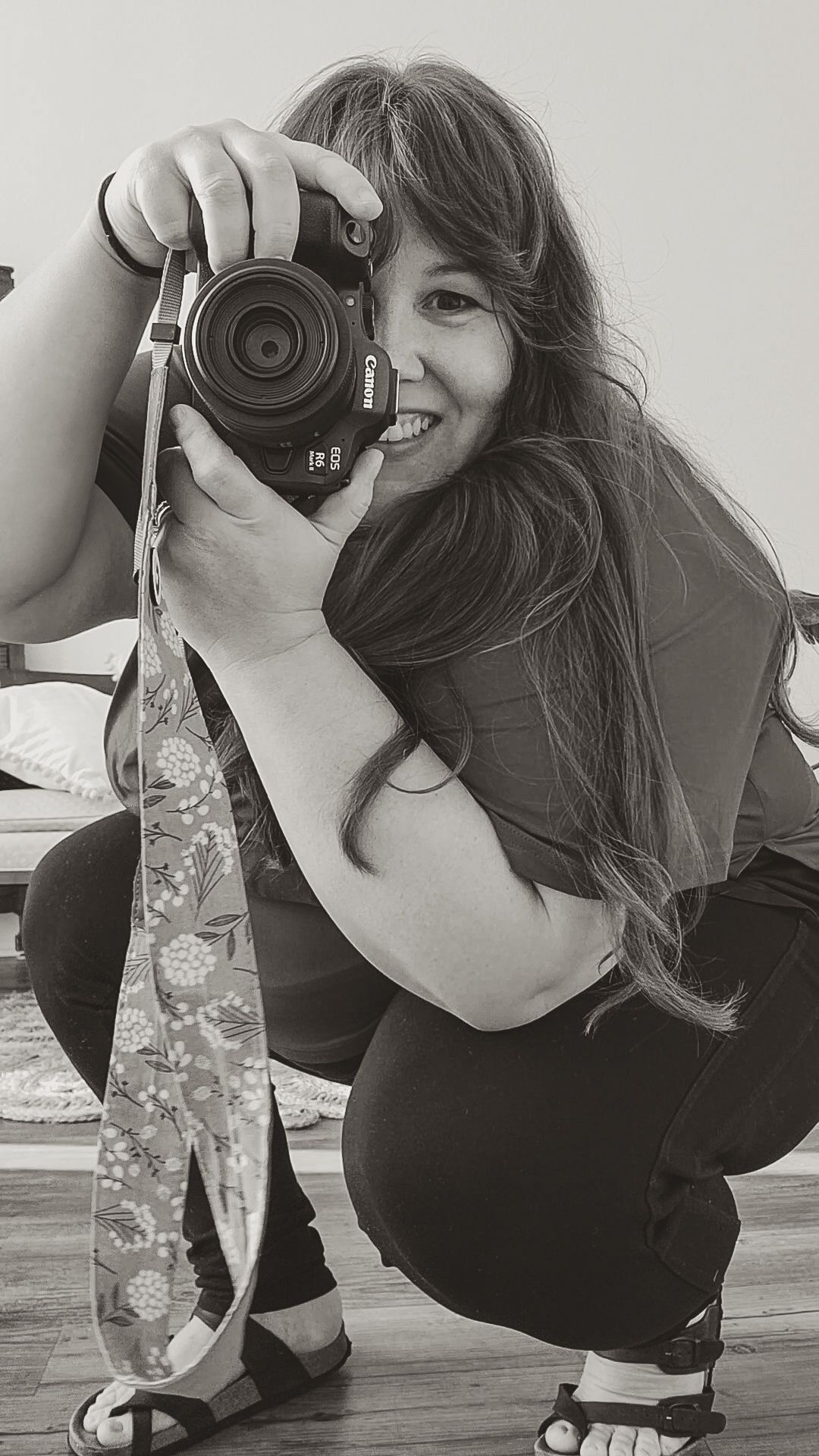 A photographer in black crouches while taking photos with a professional camera.