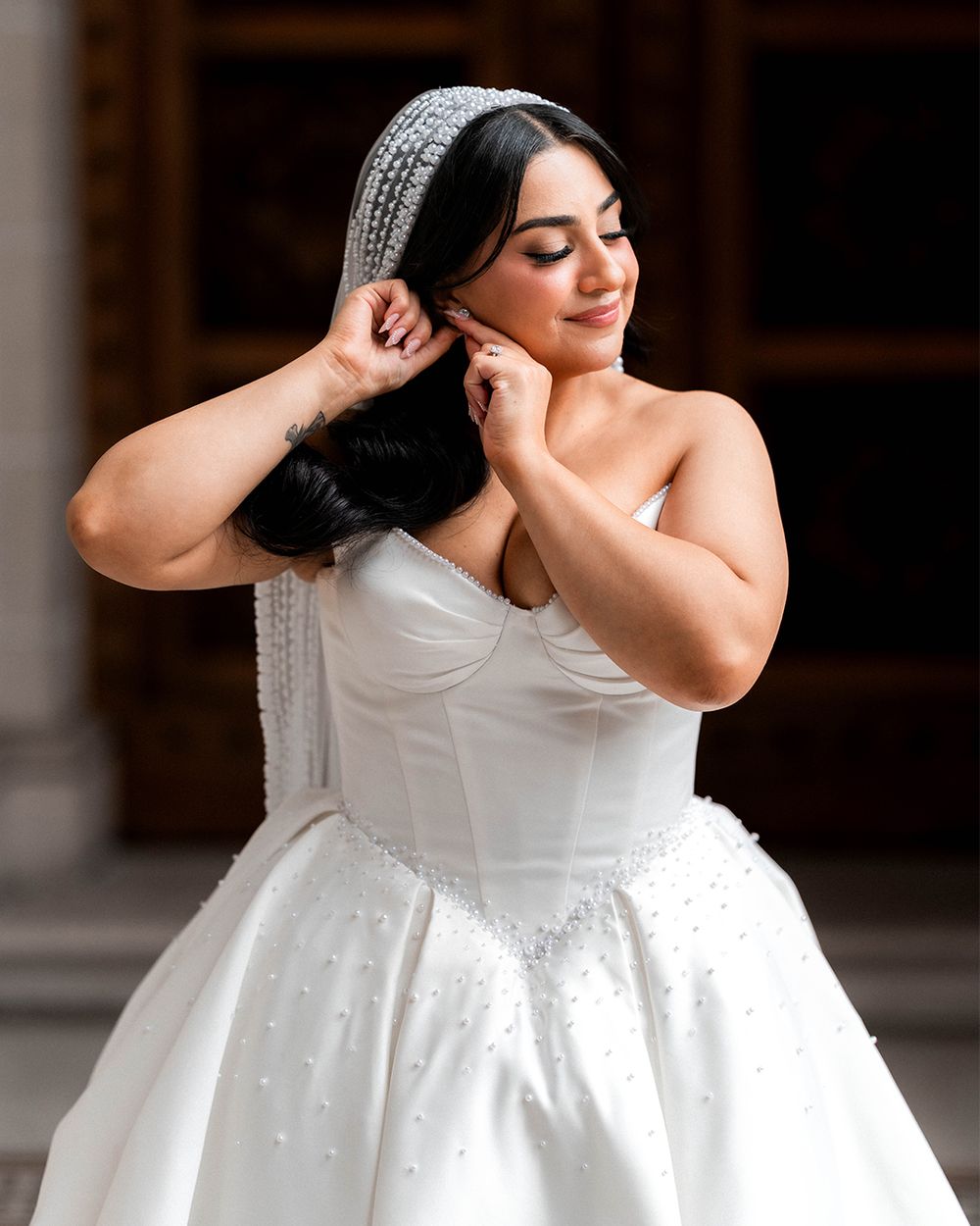 A bride in a white ball gown wedding dress poses elegantly against a dark background.