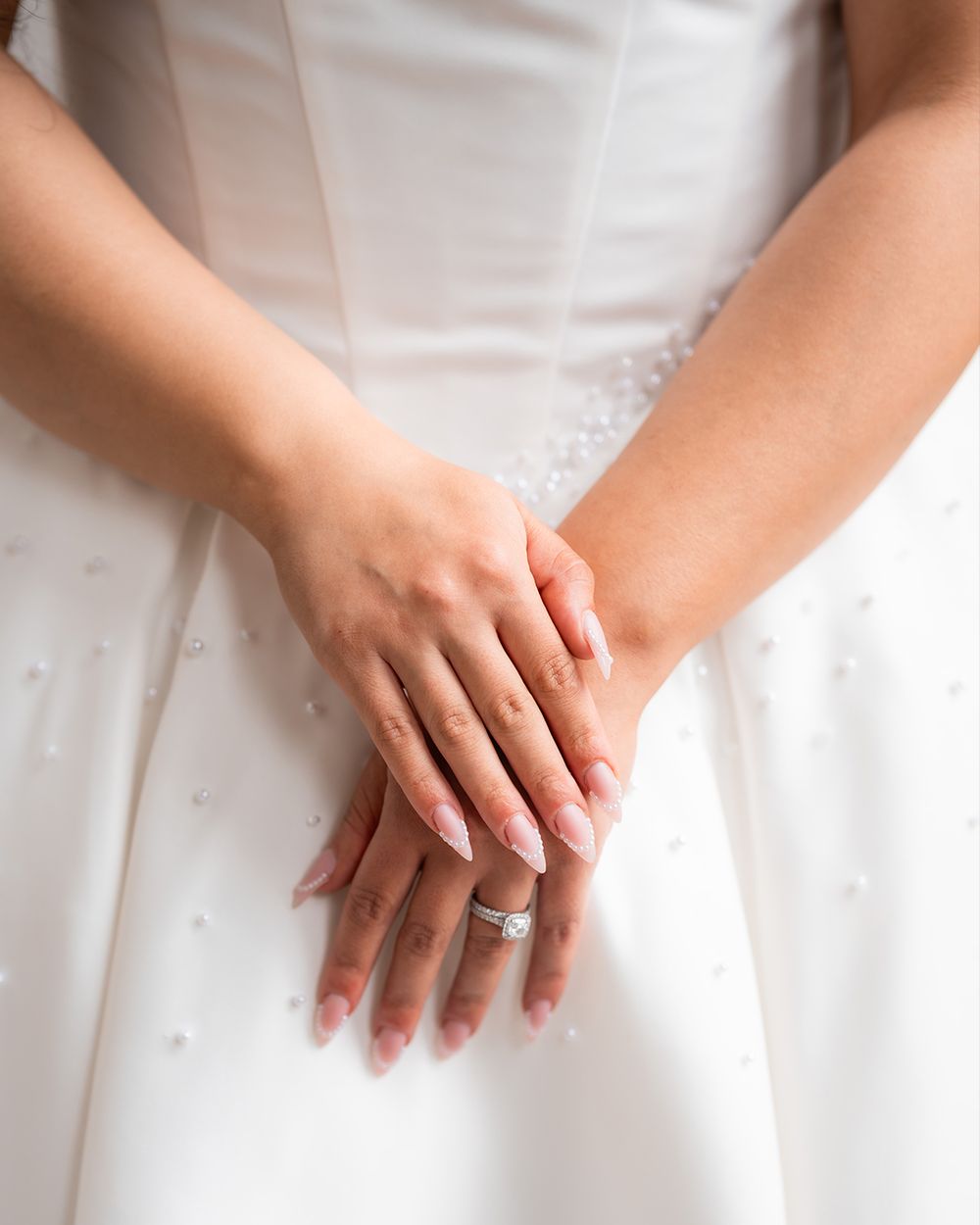 Several pairs of hands rest gently on white fabric, creating an elegant and delicate composition.