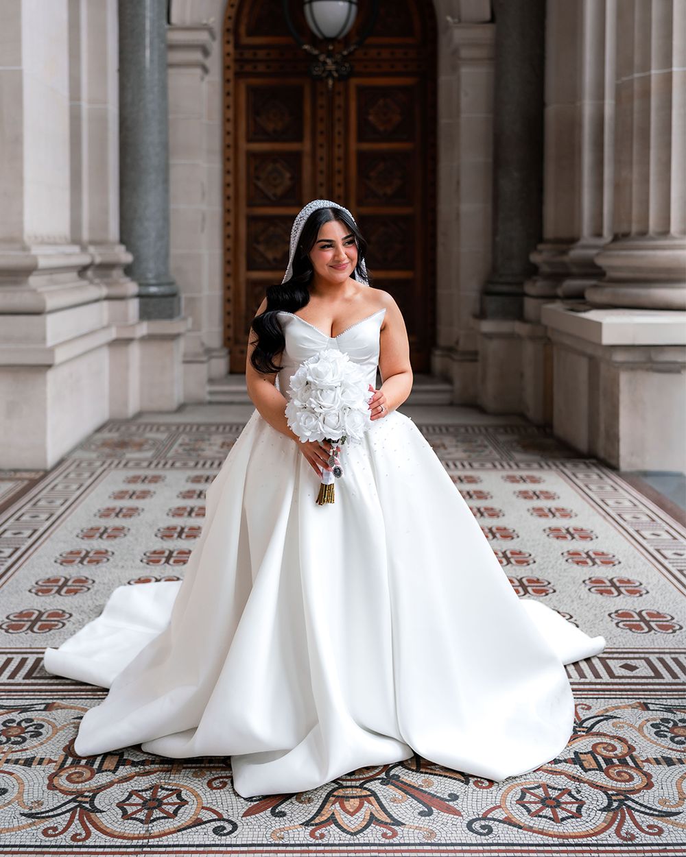 A bride in a white ballgown twirls on an ornate tiled floor in a grand historic building hallway.