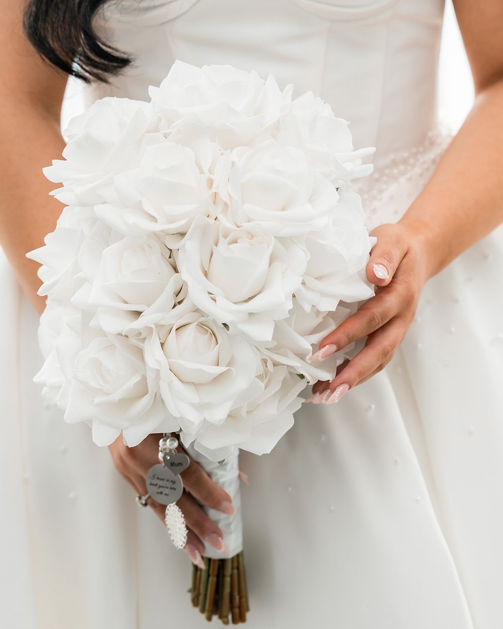 A stunning white bridal bouquet featuring full roses and delicate petals wrapped with a silver ribbon.