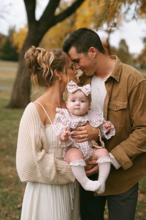 Autumn family photoshoot with parents and infant among fall foliage.