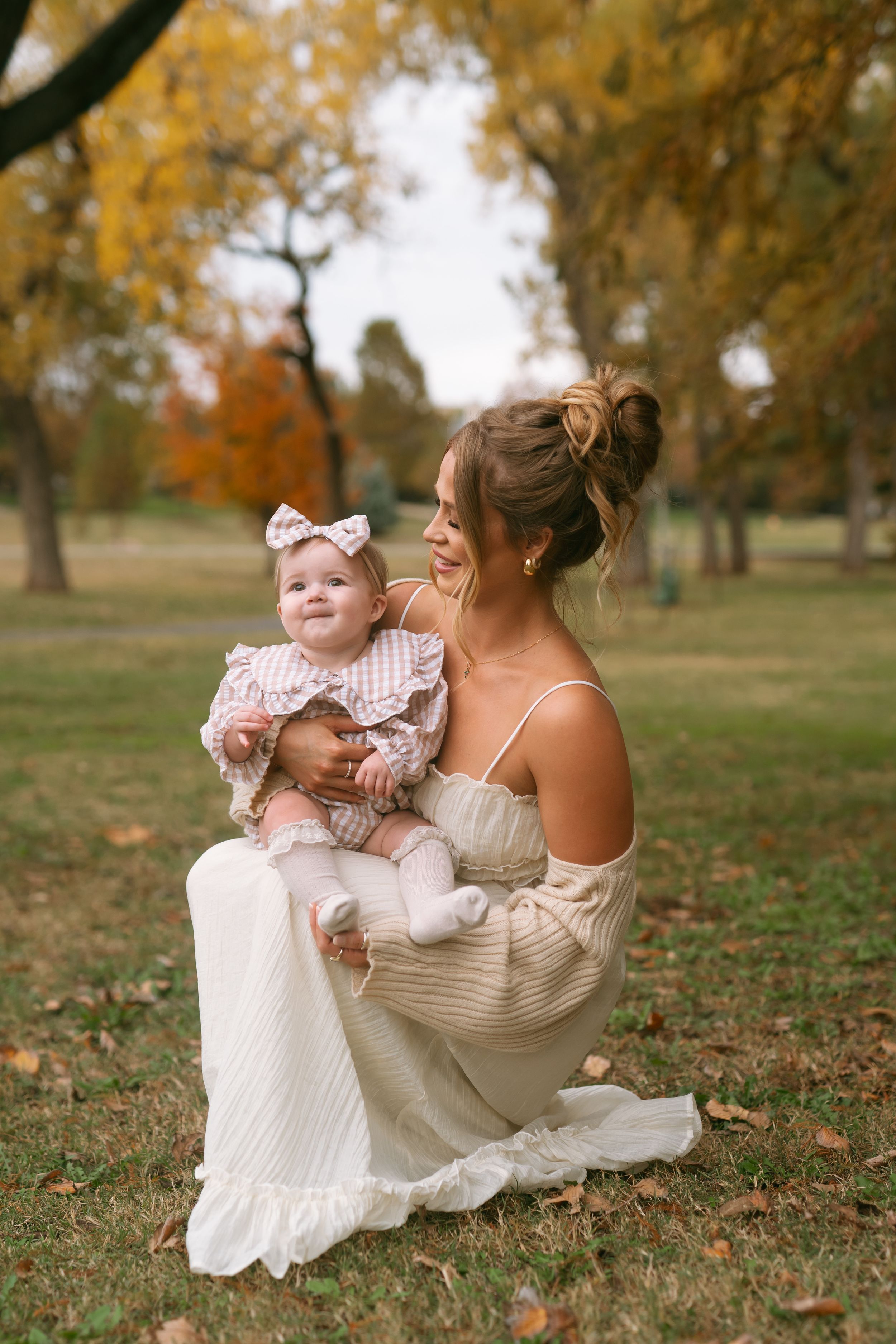 Family portrait series on autumn grass with mother in white dress and infant in pink outfit.