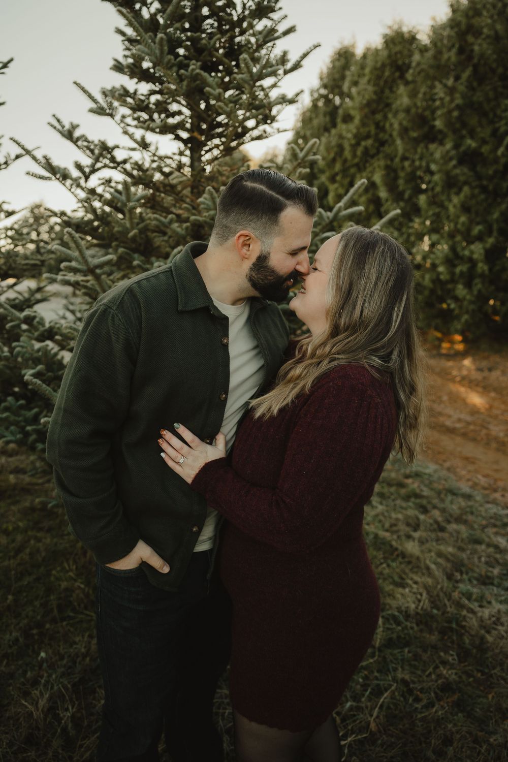 Romantic couple sharing intimate moment among evergreen trees at dusk.