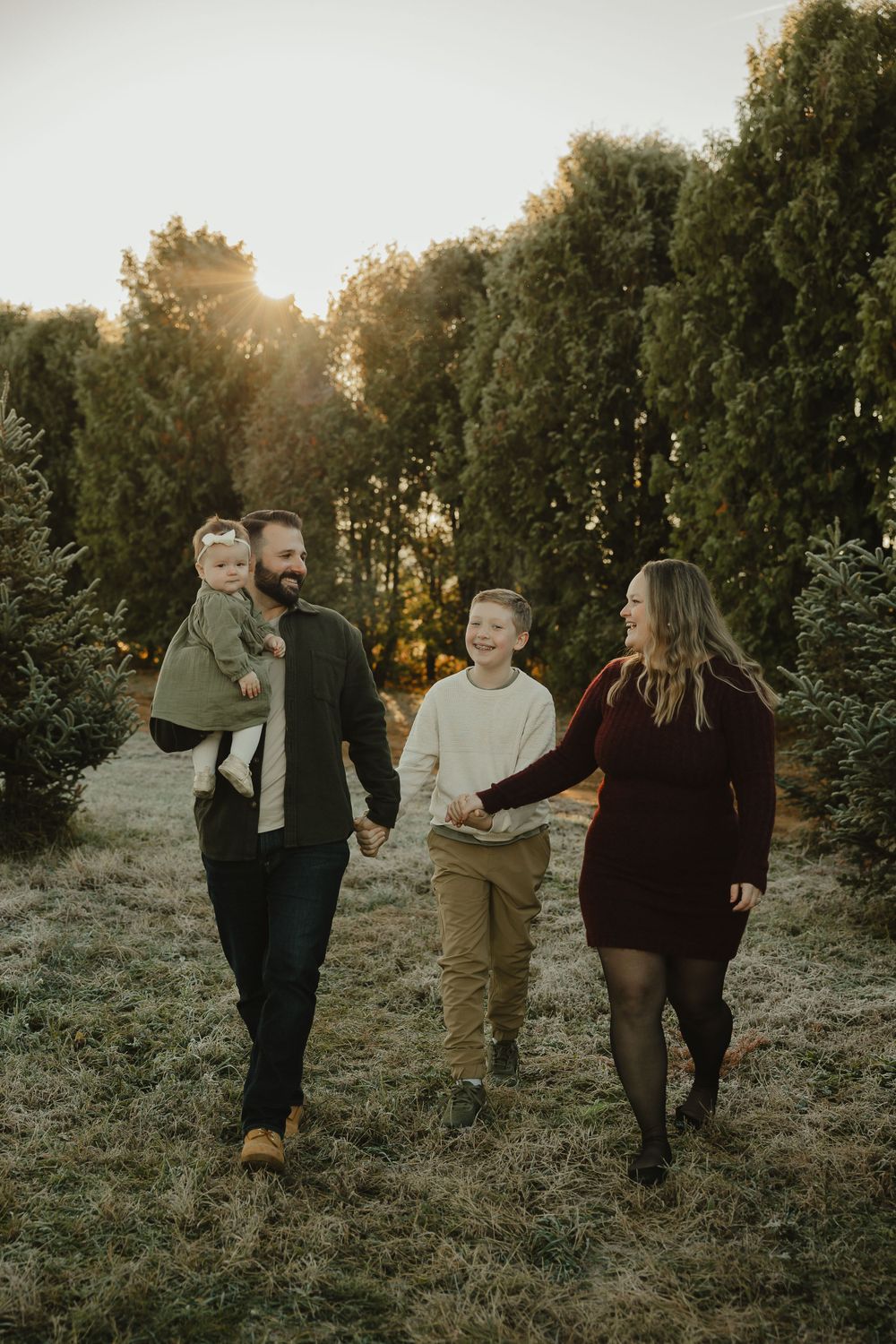 Family walking together through tree farm at golden hour.