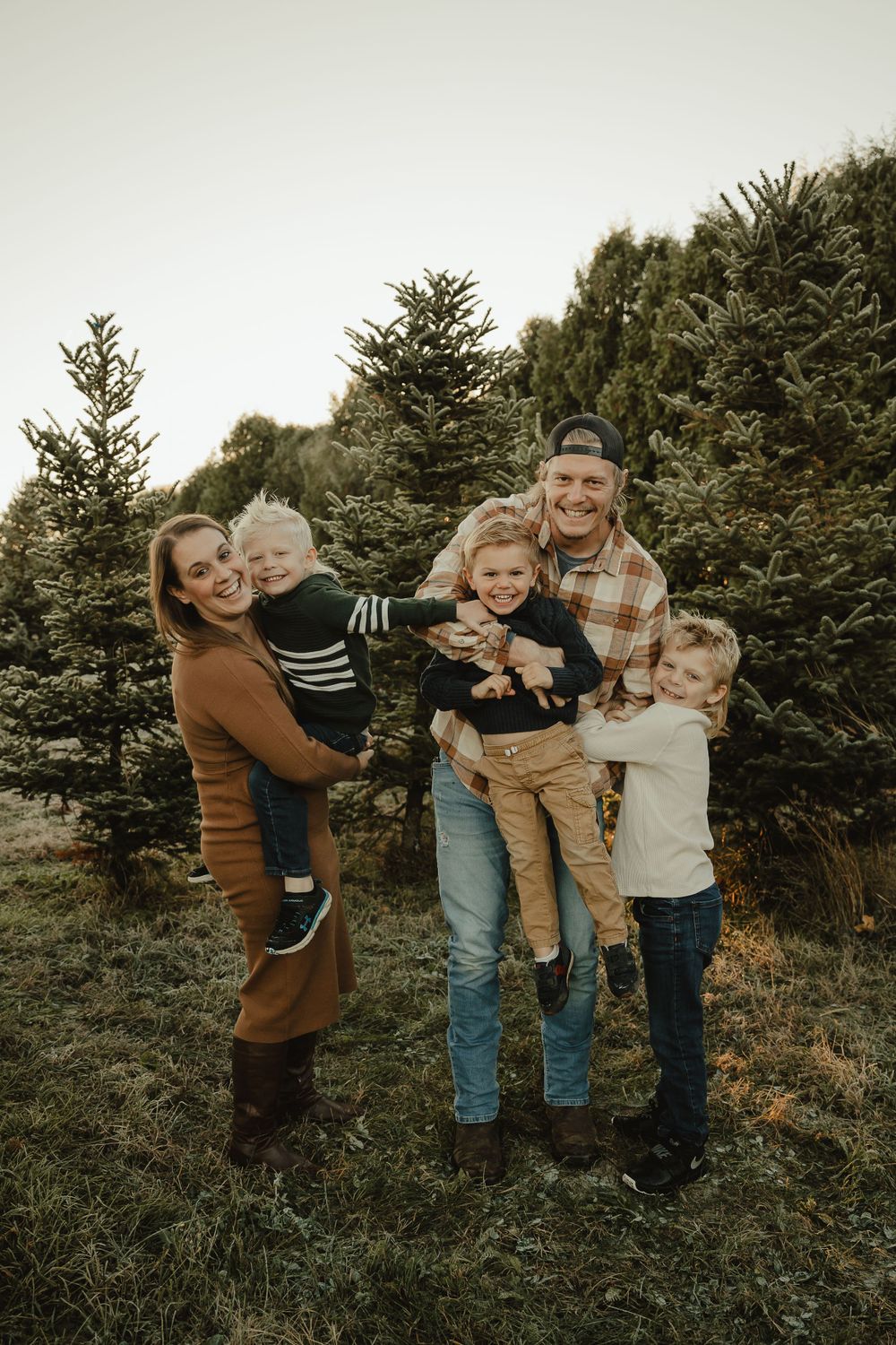 A playful family photoshoot outdoors amongst evergreen trees in warm autumn light.