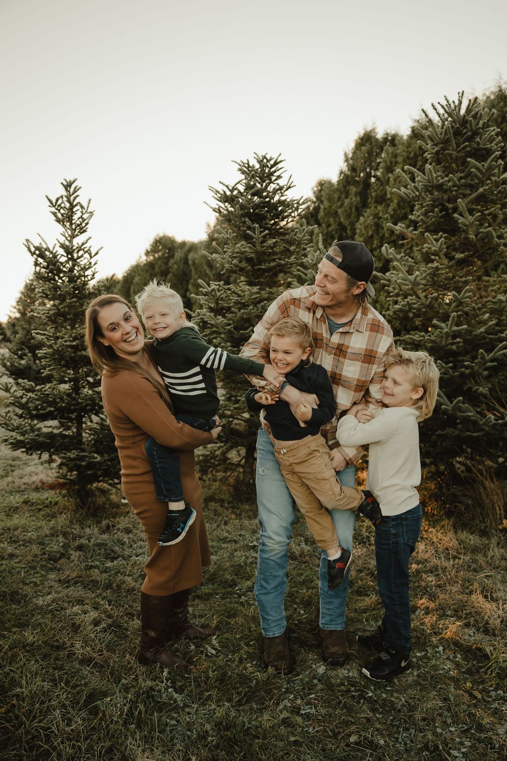 A candid family moment filled with laughter among pine trees during a golden sunset.