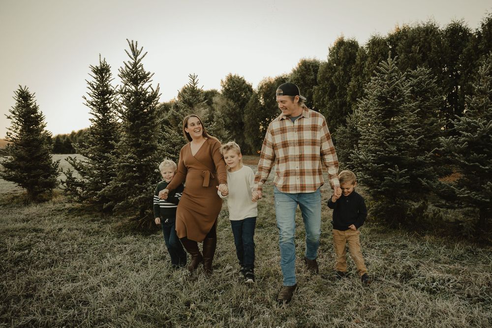 A family strolls hand in hand through a Christmas tree farm at sunset.
