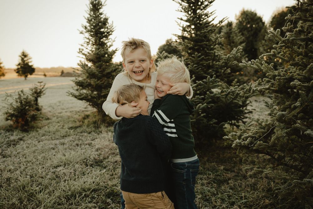 Two children laughing and playing together outdoors among evergreen trees.