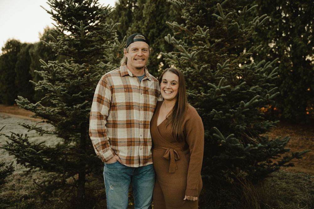 Intimate couple portrait against evergreen trees in autumn with rustic plaid and brown outfits.