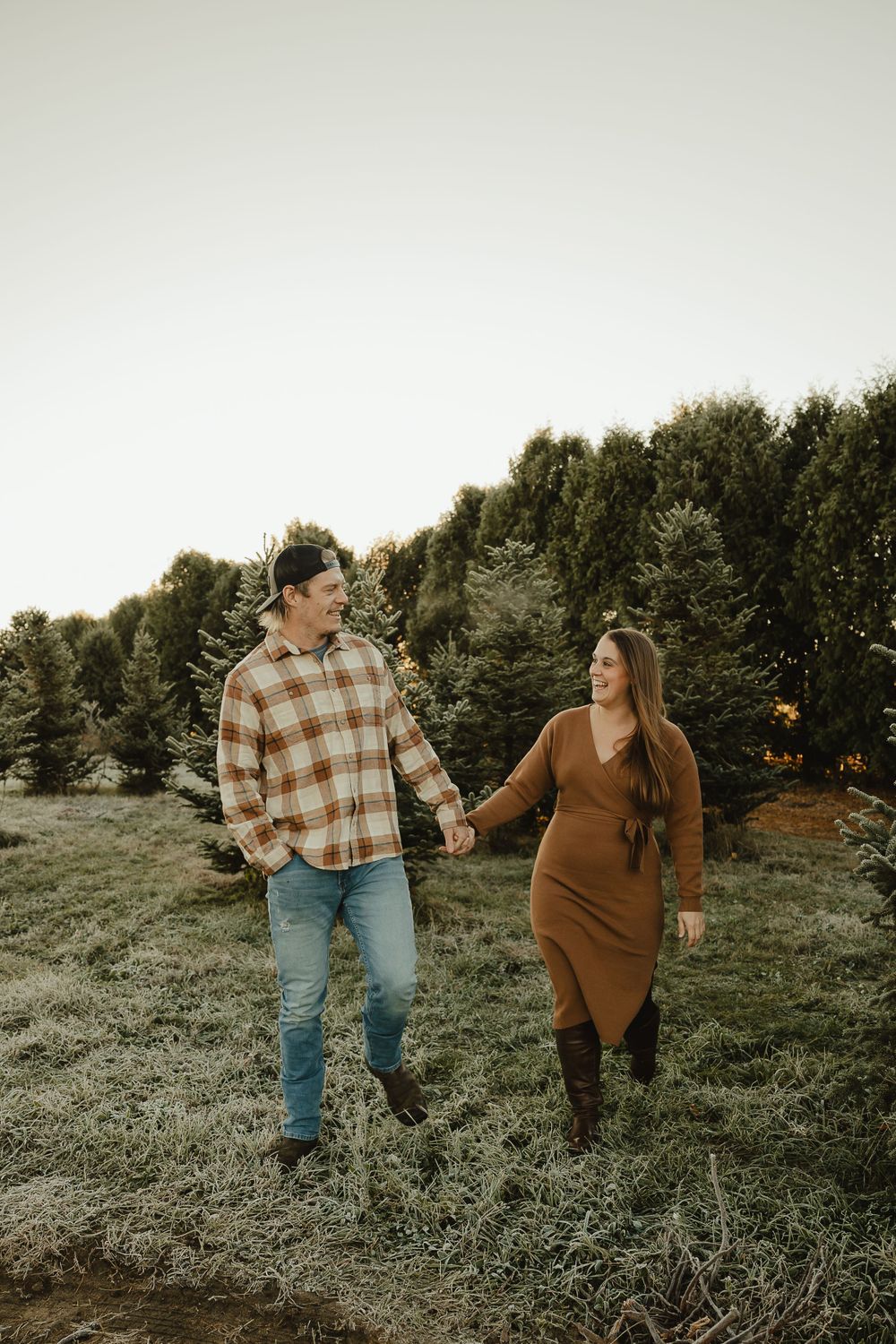 Couple walking hand in hand through a scenic evergreen tree farm at golden hour.