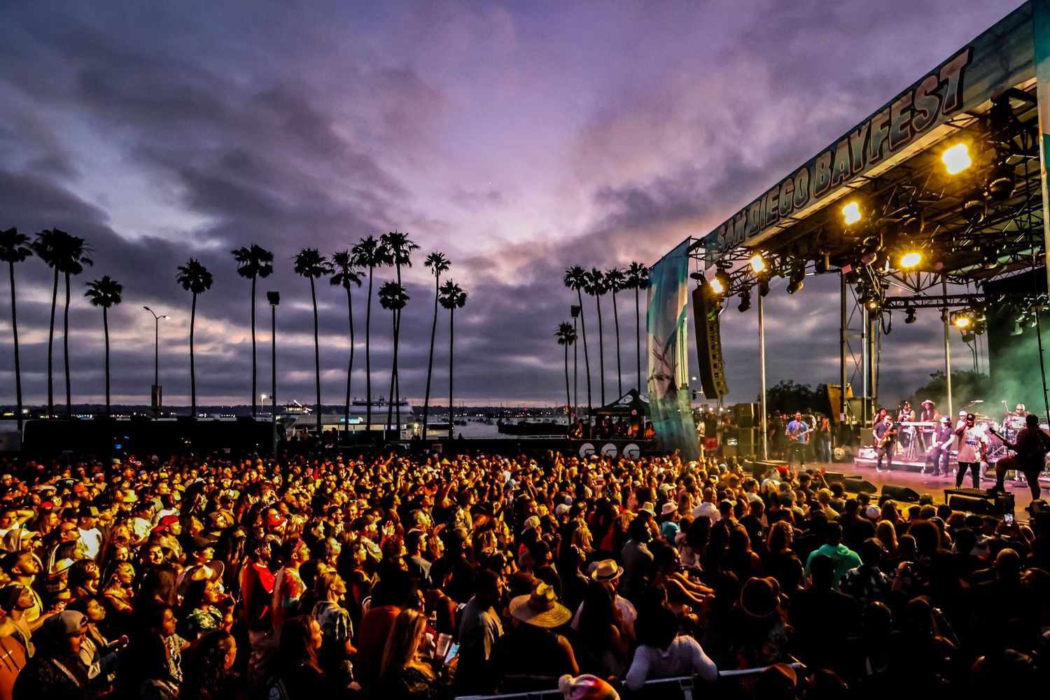Music festival photography at San Diego Bayfest, showing a large crowd watching a live concert stage at sunset with palm trees.