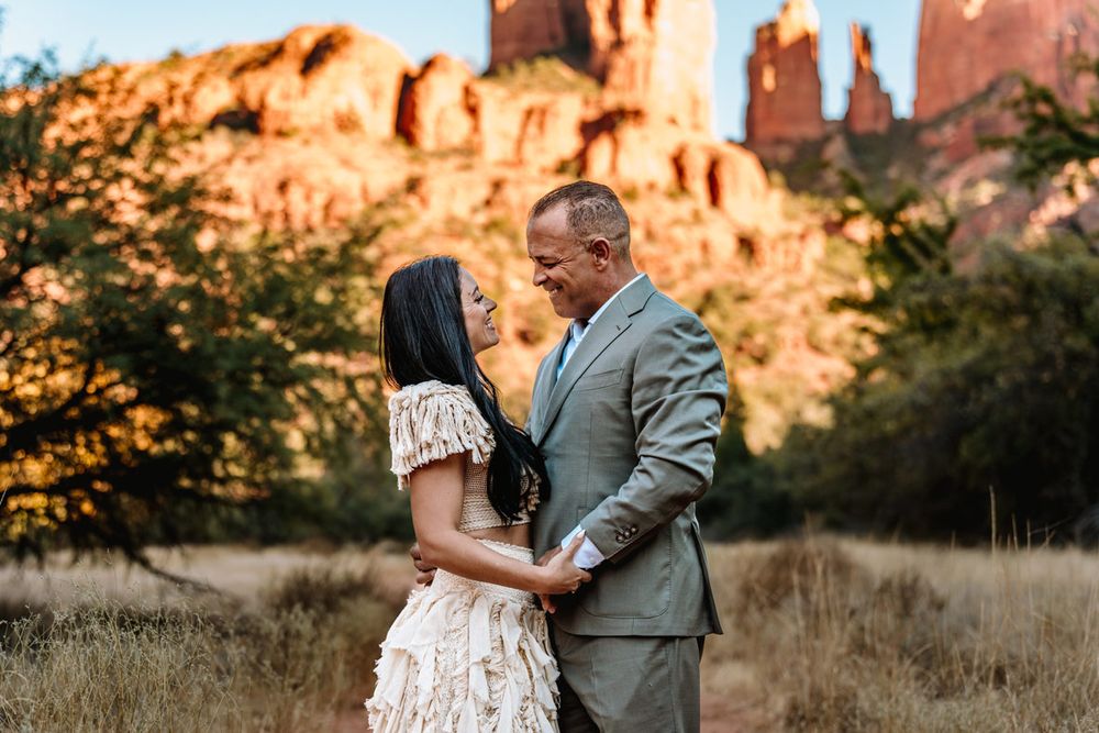 Couple sharing romantic moment with towering Sedona red rock formations in background.