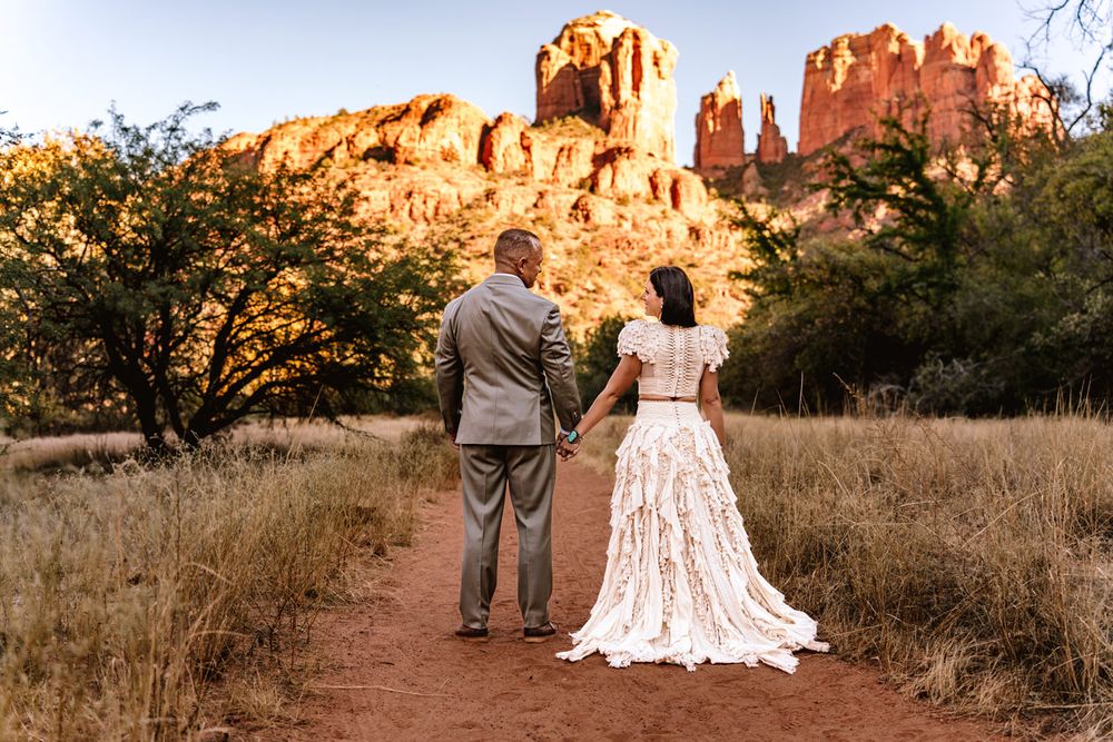 A couple in wedding attire views majestic Sedona red rock formations while standing on a desert trail.
