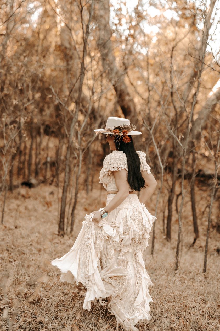 A woman in a vintage-inspired white dress twirls in a sepia-toned wooded setting.