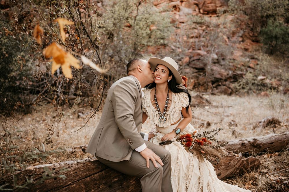 A couple shares an intimate moment while sitting on a log against Sedona red rock canyon walls.