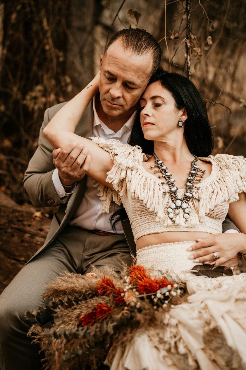 A romantic western-inspired couple embraces in vintage attire with dried floral bouquet.