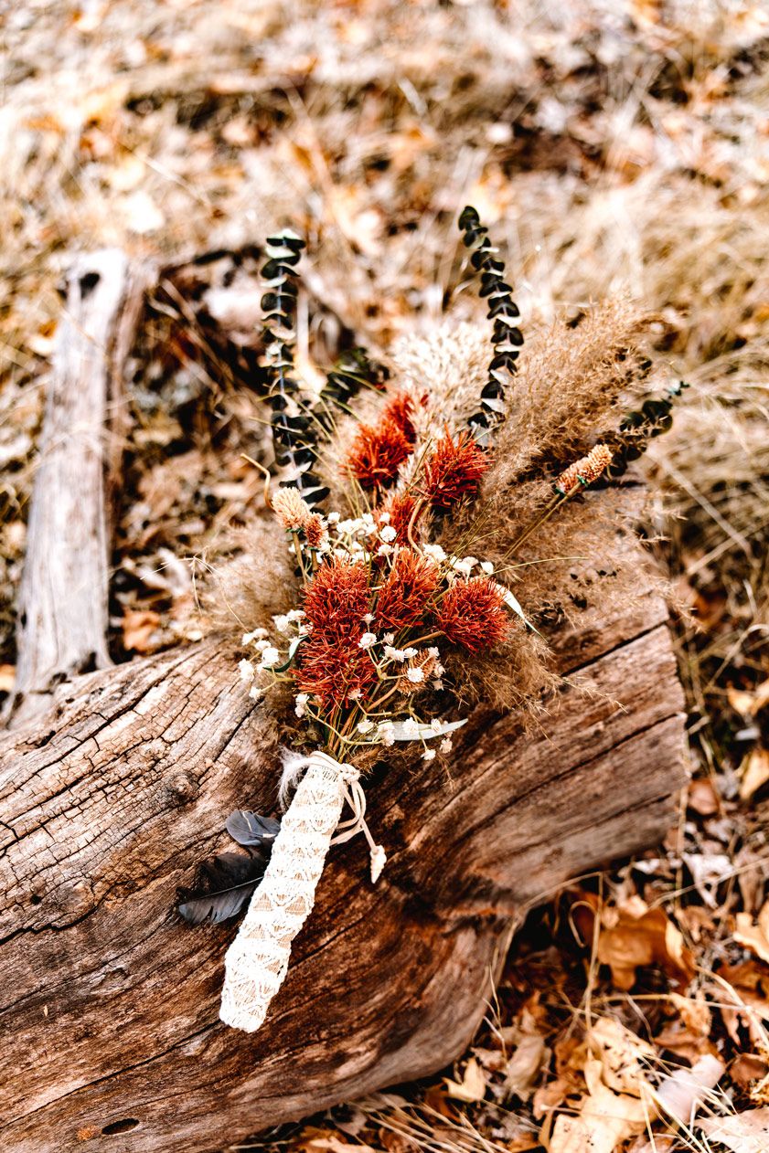A rustic dried flower bouquet with Sedona red and brown blooms rests on weathered wood.