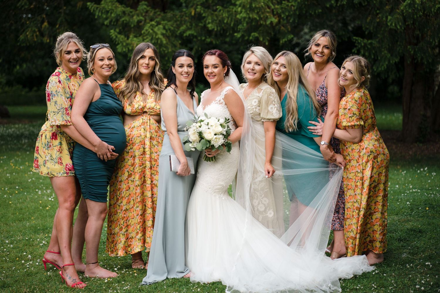 A bridal party poses outdoors in the Annapolis Valley wedding wearing mix of gold sequin and light blue dresses with white floral bouquet.