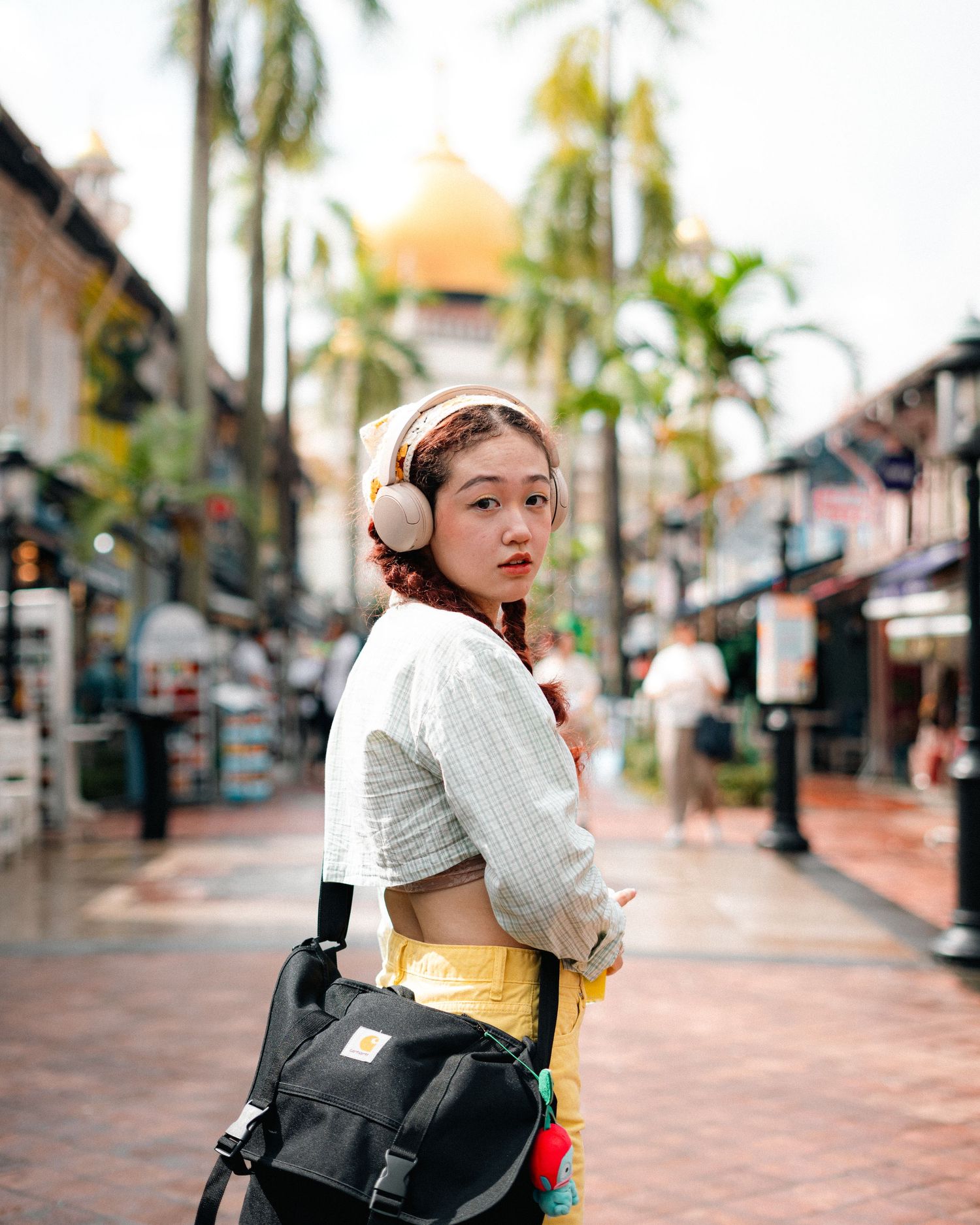 Street fashion photo with backpack and headphones against tropical palm trees and buildings.