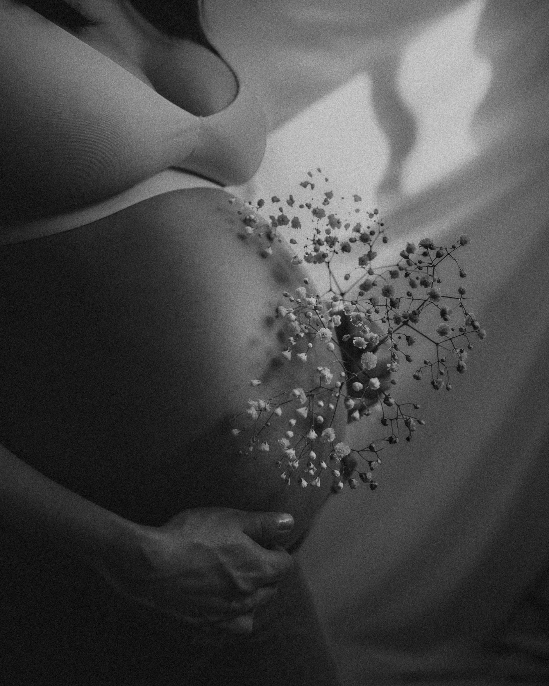 A black and white photo of a pregnant belly with delicate baby's breath flowers creating shadows.