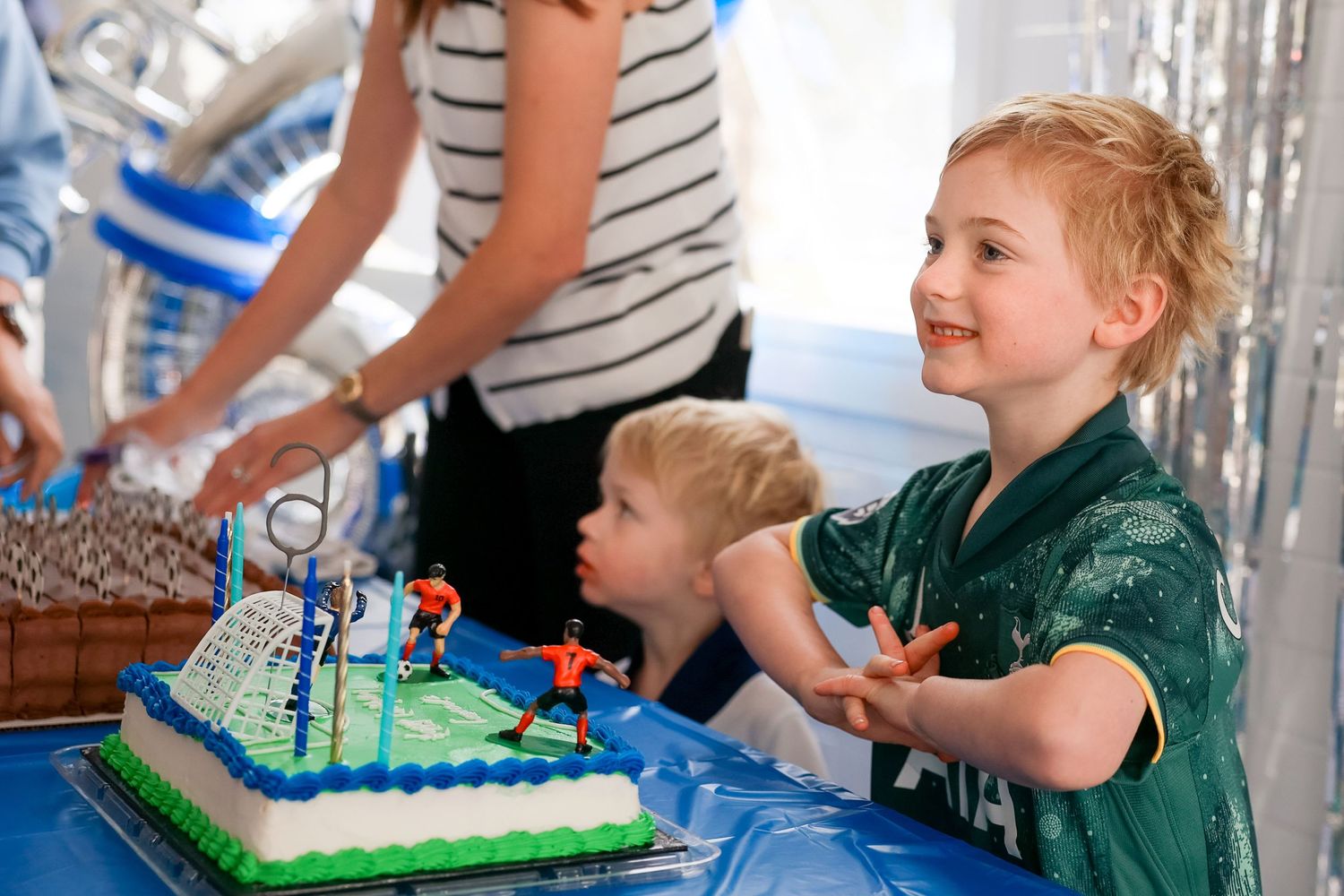 A birthday celebration with a blue-frosted cake decorated with candles at a party with festive silver decorations. By smilein Photography