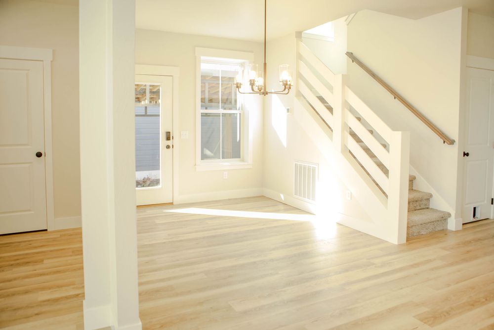 Sun-filled entryway of modern home with light hardwood floors, white walls, and stairs featuring horizontal railings.