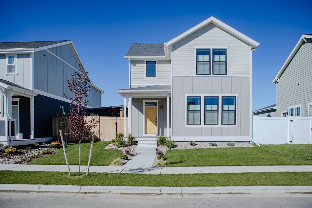 Modern two-story white farmhouse with yellow door and black windows sits on manicured lawn under bright blue sky.