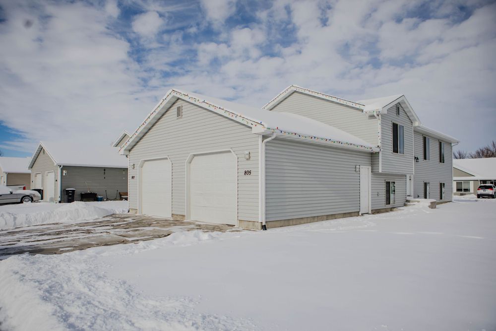White residential home with attached garage and snow covered ground under partly cloudy winter sky.