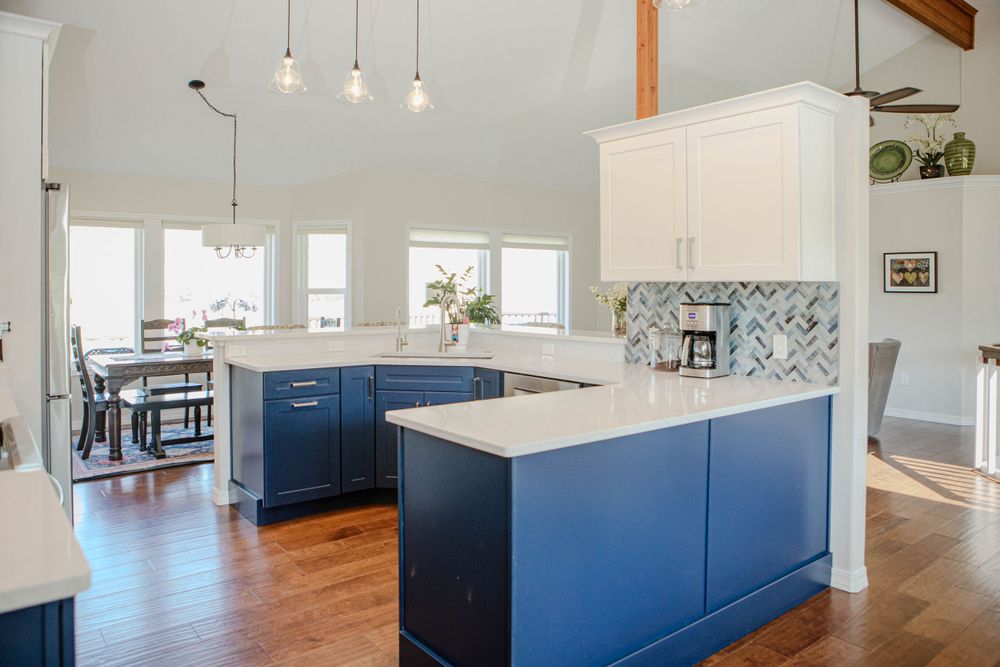 Modern kitchen with navy blue cabinets, white countertops, patterned backsplash and pendant lights in bright open space.
