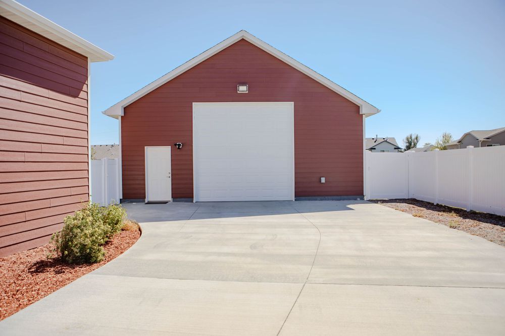 Red exterior garage building with white door and concrete driveway surrounded by red rock landscaping.