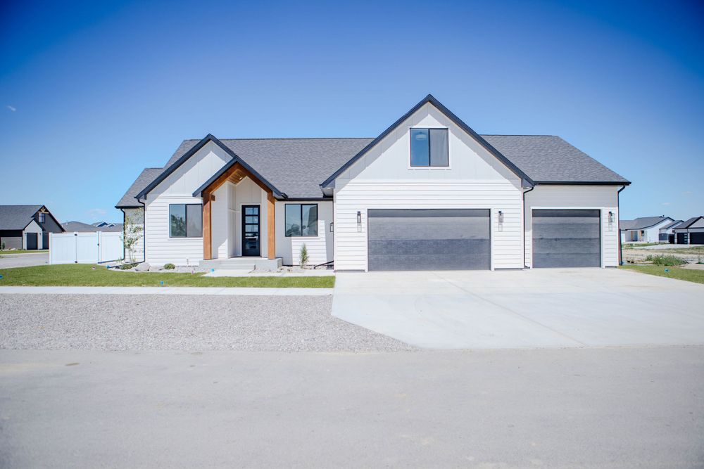 Modern gray and white ranch-style home with three-car garage and concrete driveway against blue sky backdrop.