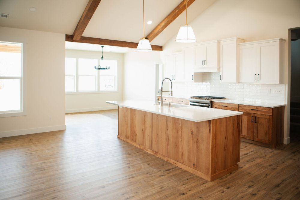 Modern open concept kitchen with wood base island, white countertops, and exposed ceiling beams in bright airy space.