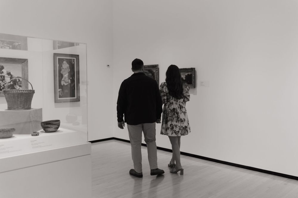 A couple explores black and white photographs in a minimalist gallery space.