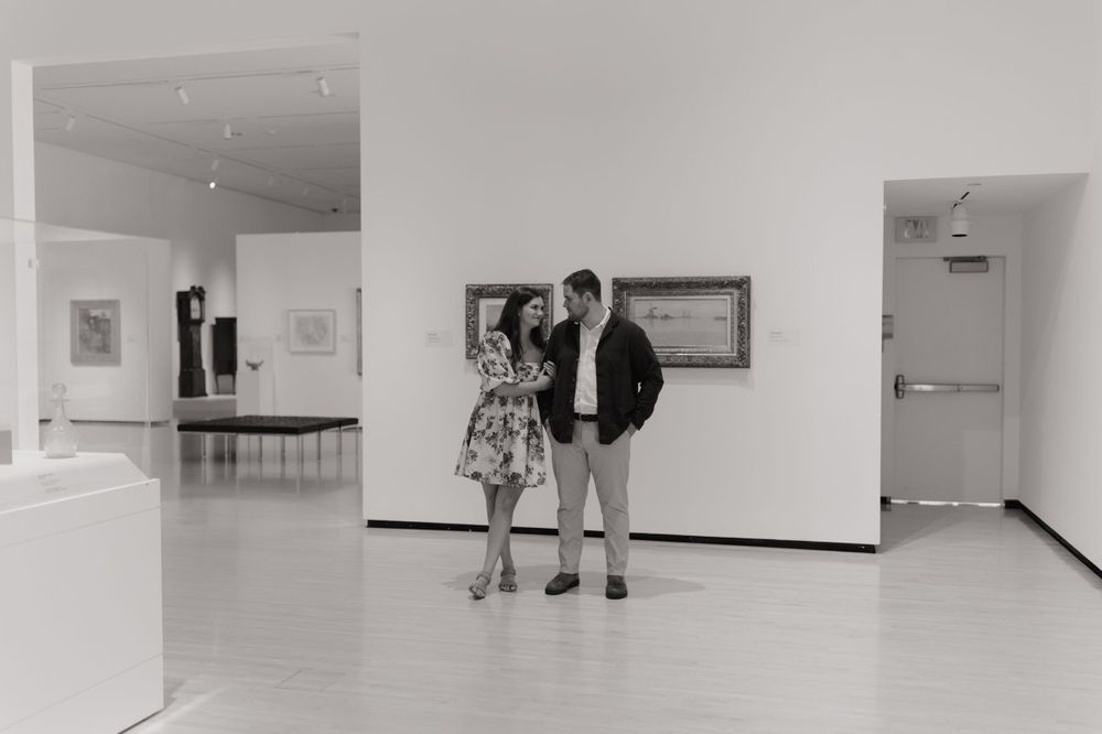 Two people view artwork in a modern white-walled gallery space.