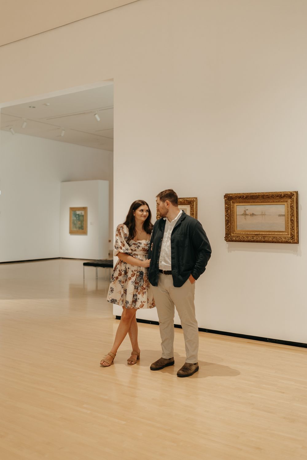 A couple in casual attire enjoys an intimate conversation in an art museum.