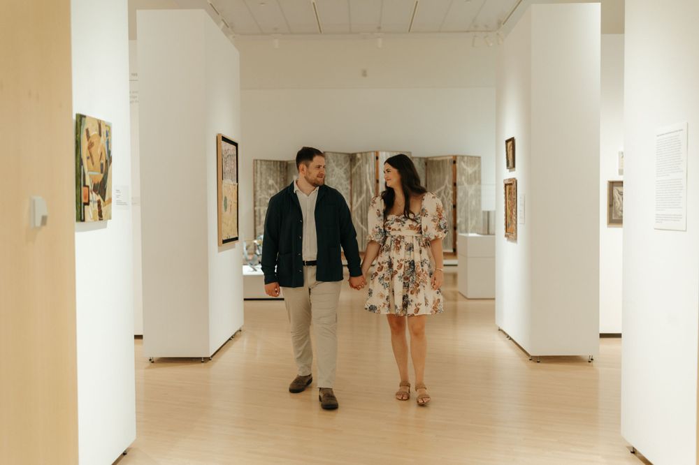 A couple walks through a bright gallery hallway lined with artwork.